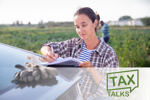 Confident female farmer standing outdoors near car on background with farm field on fall day, signing some papers