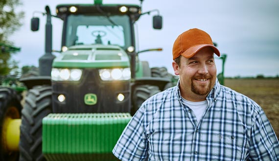 Smiling Farm Credit East customer in front of tractor after a hard day of planting