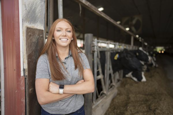 Picture of Megan Clancy, Farm Credit East Risk Advisor standing in a dairy barn with black and white cows in the background