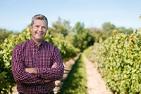 Professional portrait of Hans Walter-Peterson standing in a field of grape vines on a sunny day