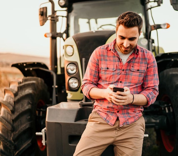 Smiling farmer taking a break to check his online account from his phone 