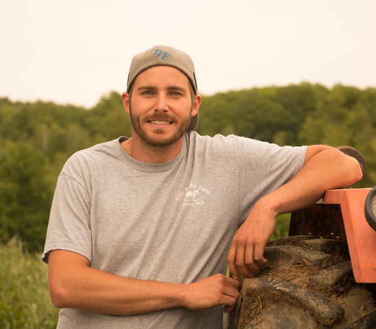 Man in T-shirt and backward hat leans on a tractor