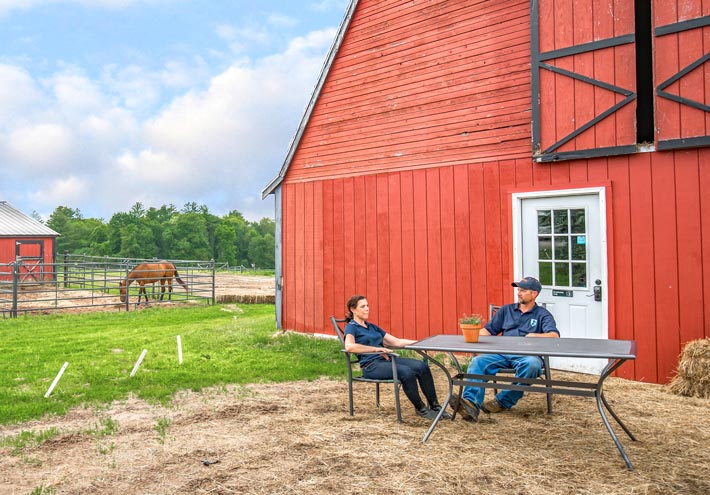 Ron and Nancy Robbins of North Harbor Dairy squat down by a lineup of their dairy cows eating