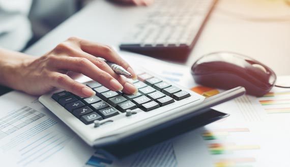 Close-up of female’s hand typing on calculator and reviewing tax documents 