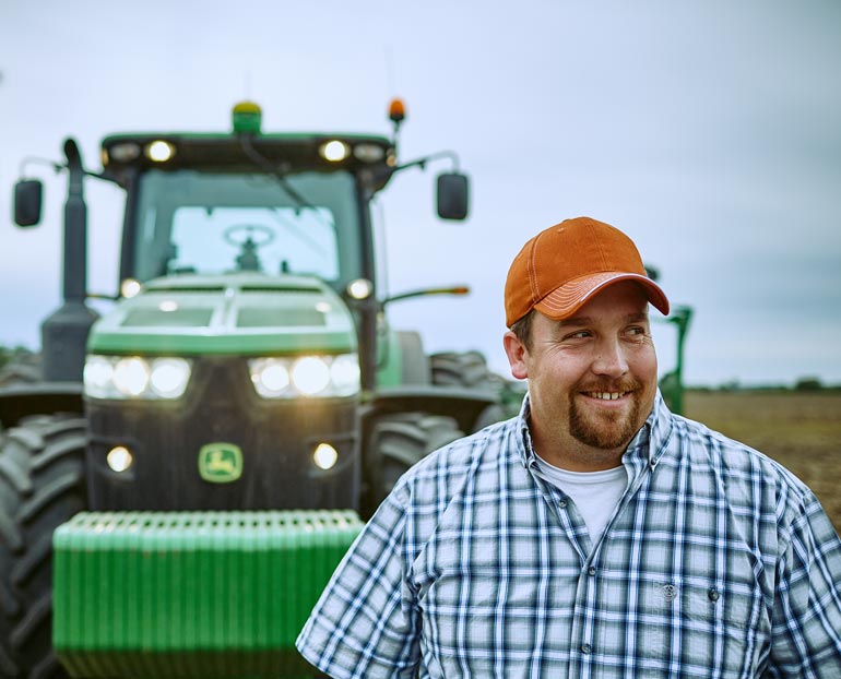 Smiling Farm Credit East customer in front of tractor after a hard day of planting 