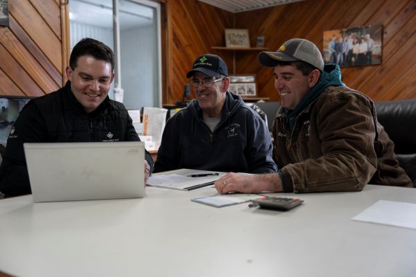 Three men sitting at a table talking and looking at a laptop