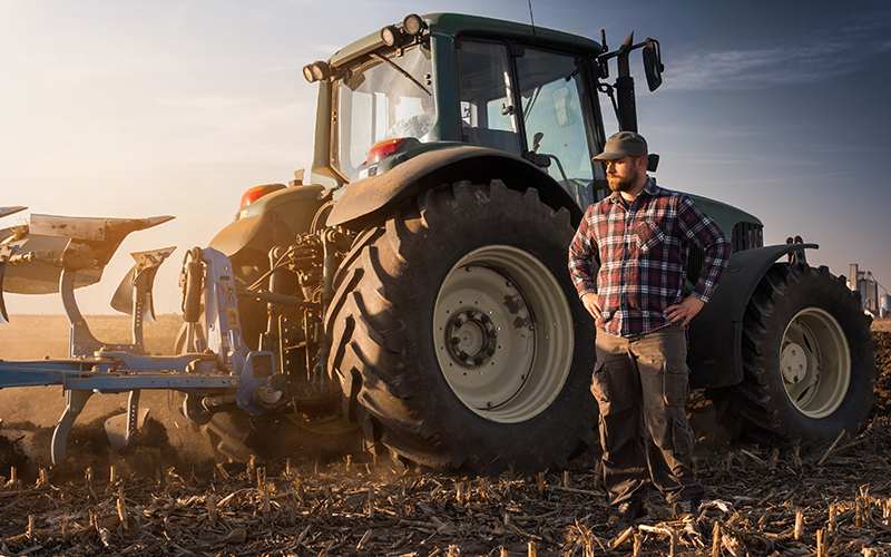 Male farmer standing in front of tractor and plow