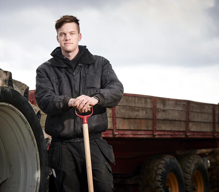 Young farmer smiling in front of ag equipment 
