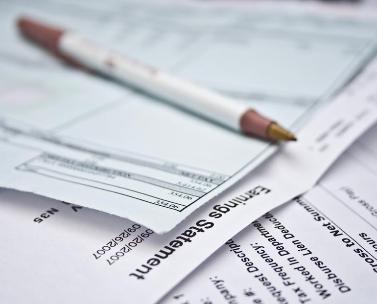 Close-up of female’s hand typing on calculator and reviewing tax documents