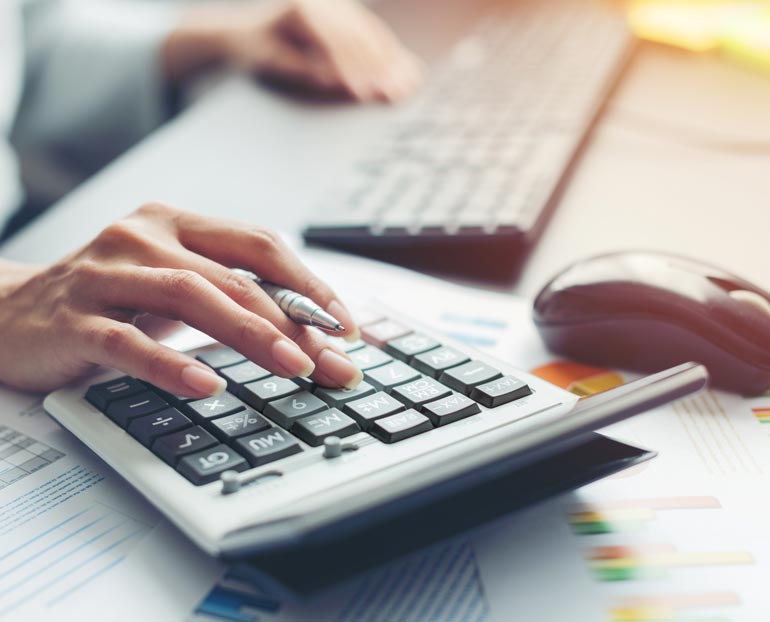 Close-up of female’s hand typing on calculator and reviewing tax documents 